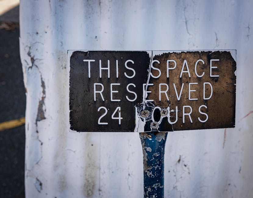 A circular no parking sign with a red border and a black letter 'P' crossed out by a red diagonal line, mounted on a grey metal pole against a plain grey sky background. The sign is positioned outdoor